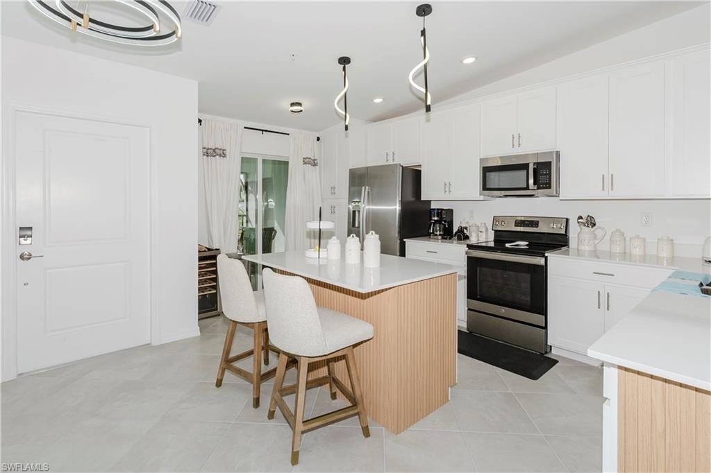 Kitchen with stainless steel appliances, a kitchen island, a kitchen bar, white cabinets, and light countertops