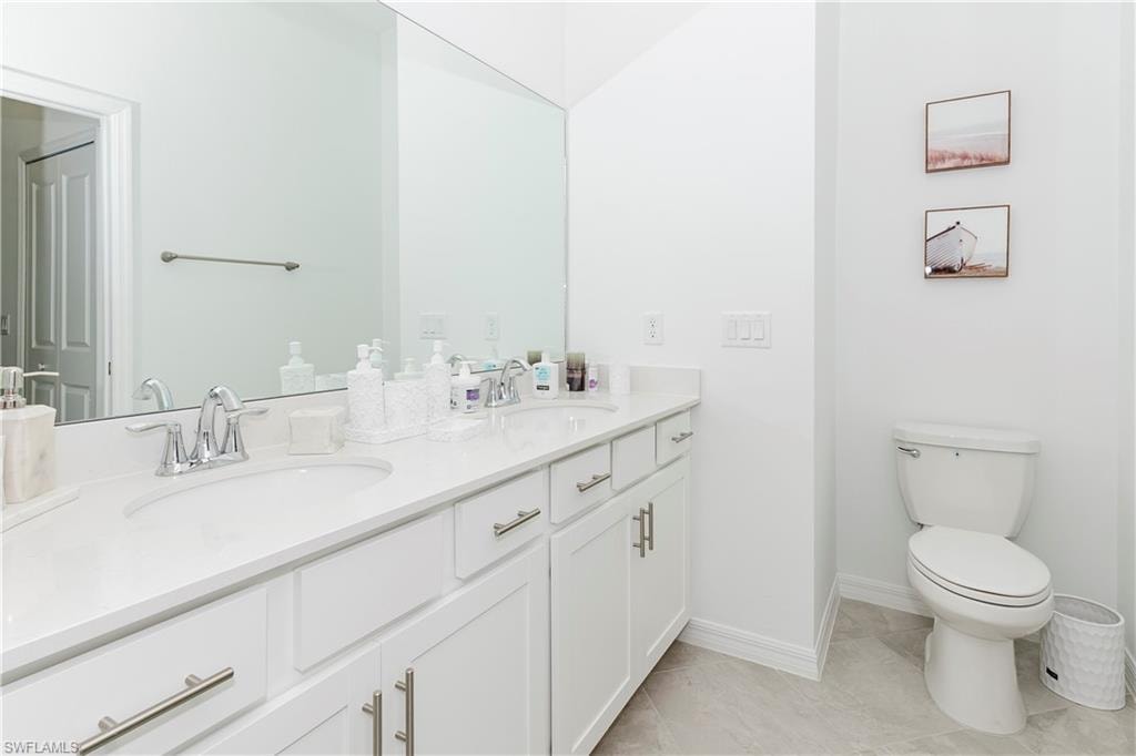 Full bath with double vanity, toilet, and baseboards