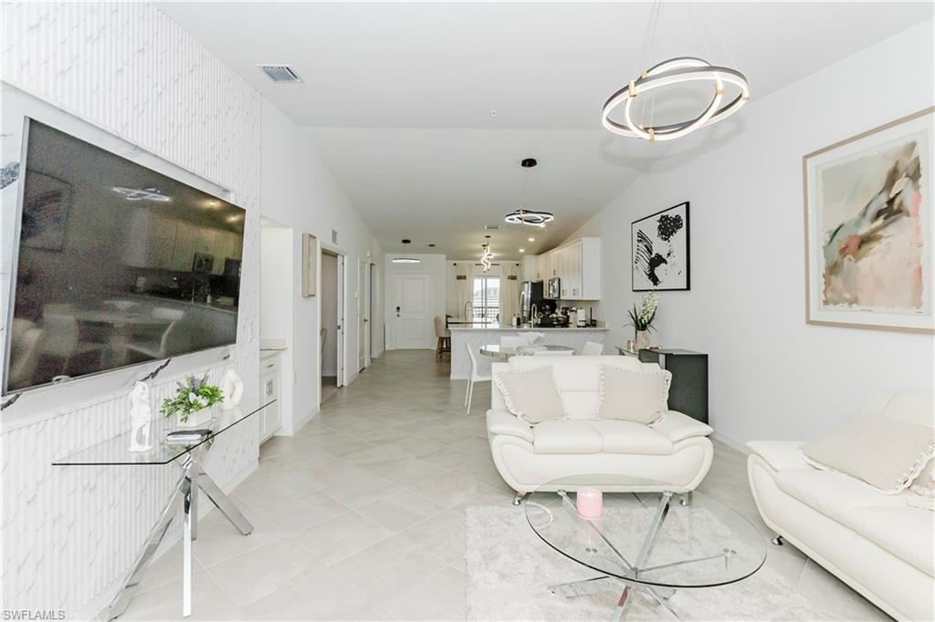 Living area with a chandelier, light tile patterned flooring, vaulted ceiling, and baseboards