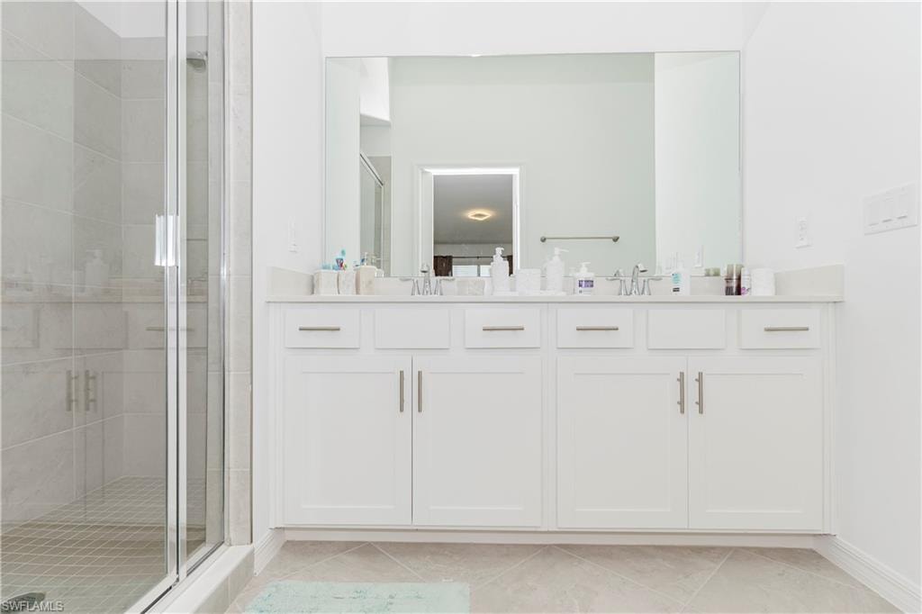 Bathroom featuring a shower stall, double vanity, and baseboards