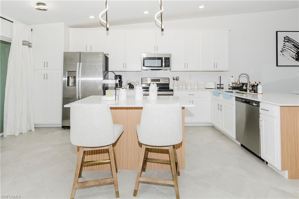 Kitchen featuring appliances with stainless steel finishes, a kitchen bar, a sink, light countertops, and recessed lighting