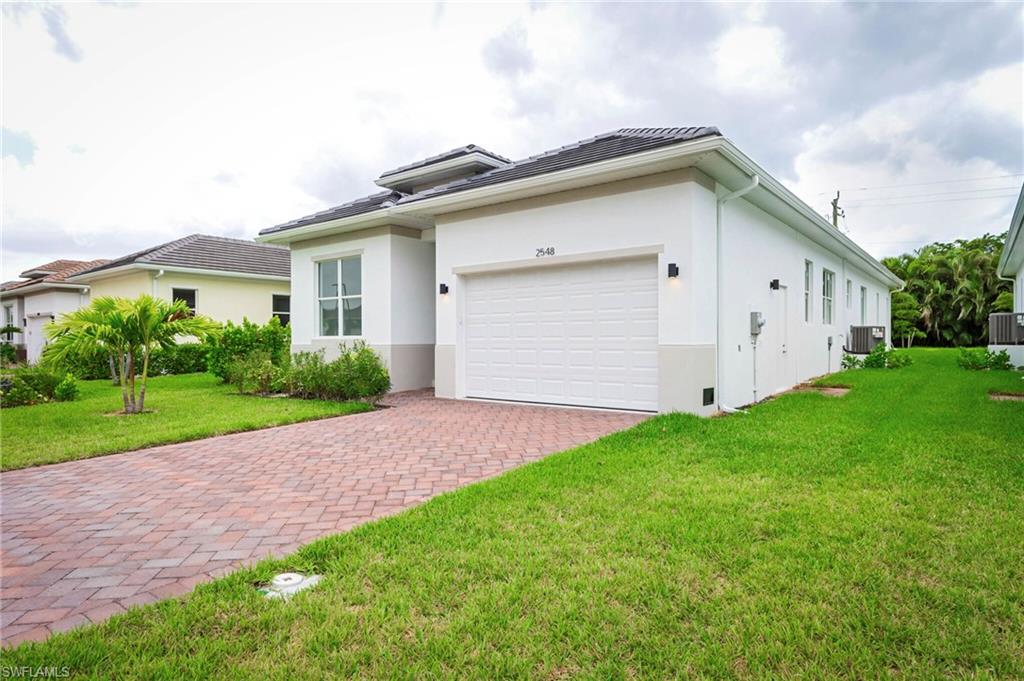 View of front facade featuring a front lawn, stucco siding, decorative driveway, a garage, and a tile roof