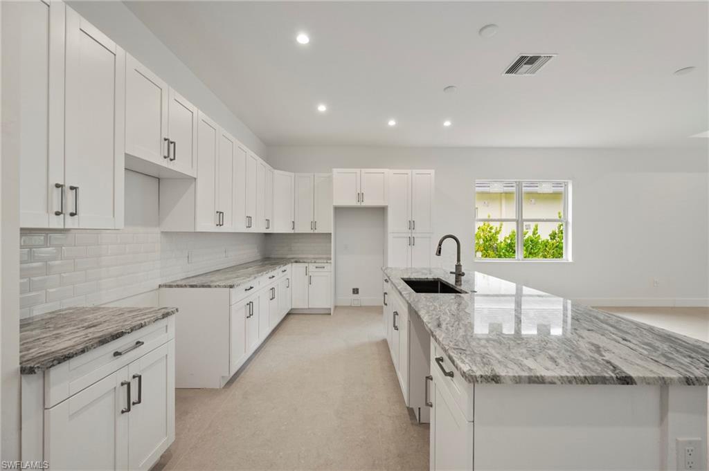 Kitchen with white cabinetry, light stone counters, recessed lighting, an island with sink, and backsplash