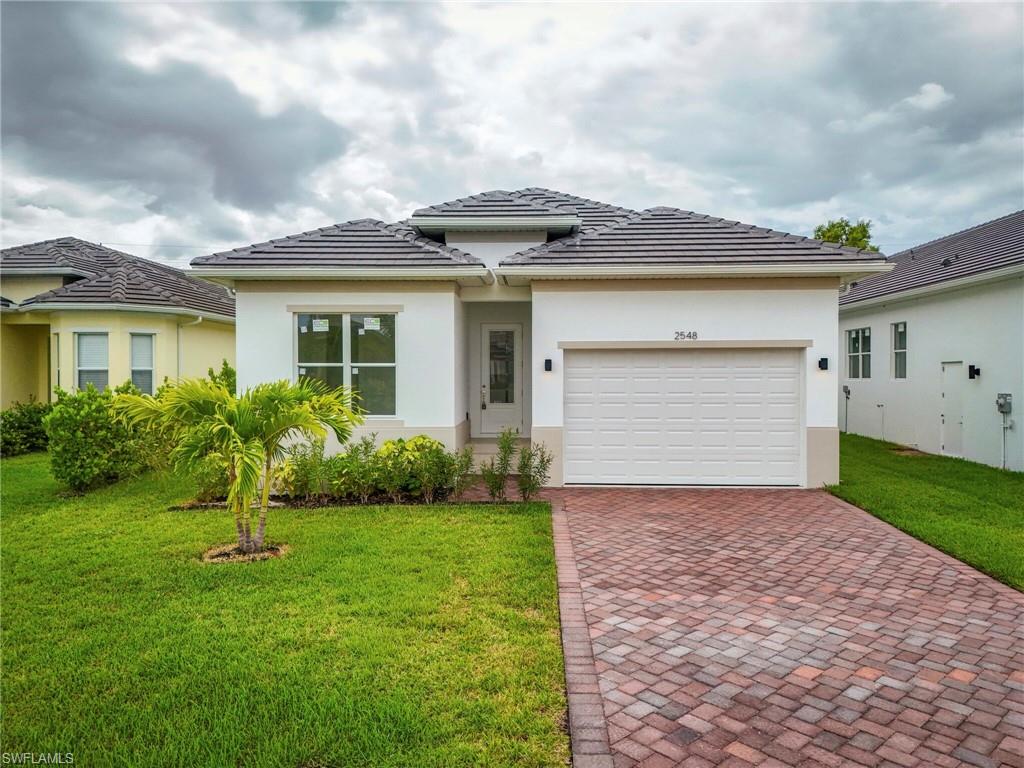Prairie-style house featuring decorative driveway, a front lawn, stucco siding, an attached garage, and a tiled roof