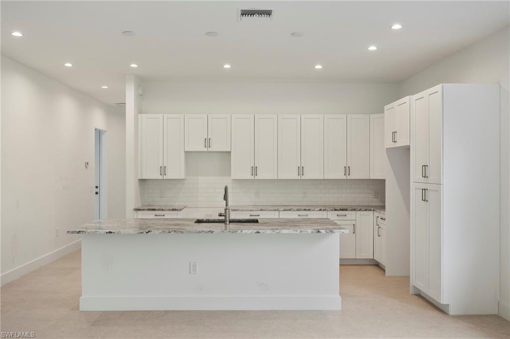 Kitchen featuring light stone countertops, white cabinetry, recessed lighting, backsplash, and an island with sink