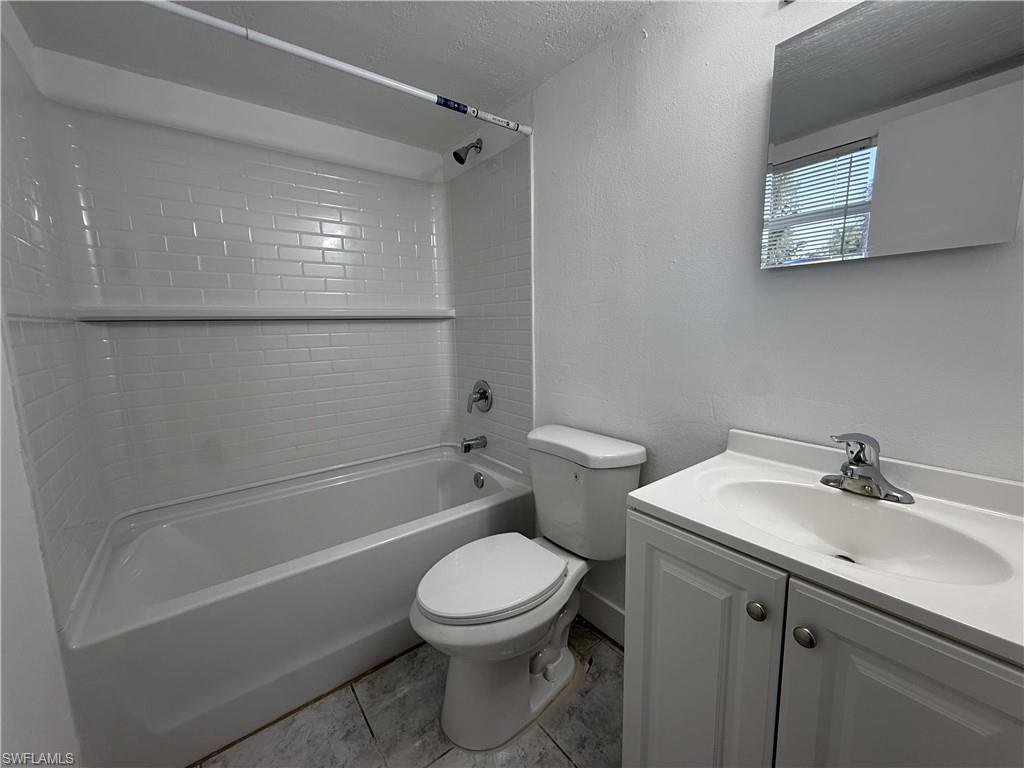 Bathroom featuring a white subway tile shower surround, a white bathtub, a toilet, a vanity with a white basin sink, and a wall-mounted mirror