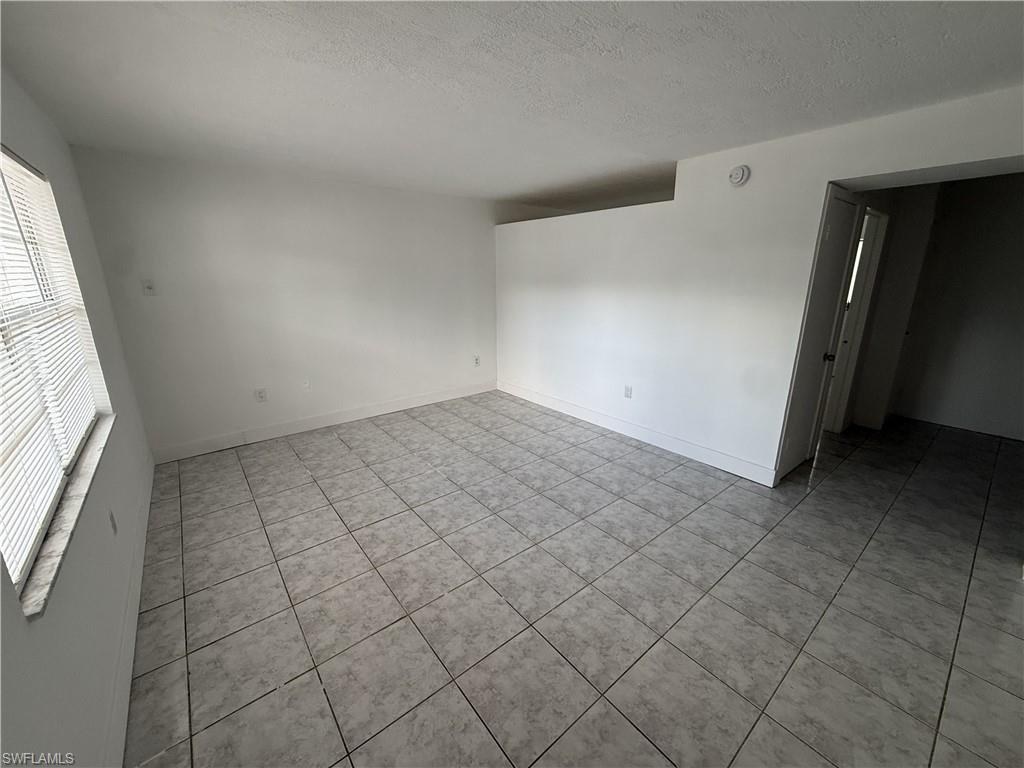 This spacious room features neutral-toned tiled flooring, white walls, and a window with horizontal blinds