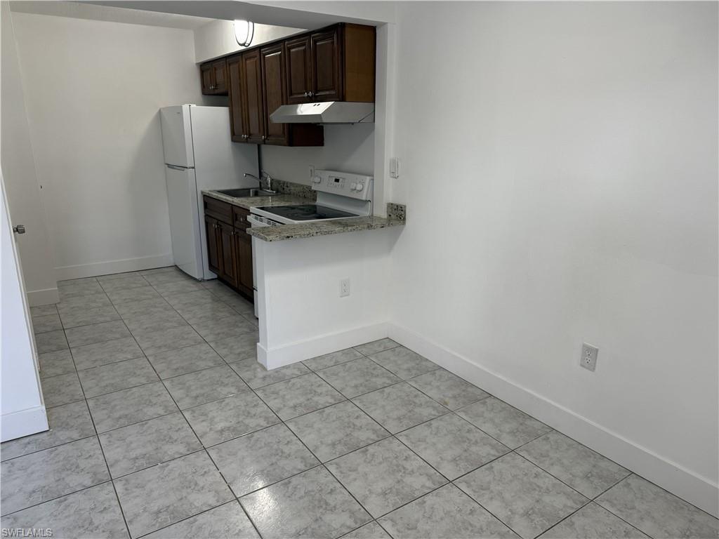 Kitchen area featuring dark wood cabinetry, a white refrigerator, a white electric range, and granite countertops