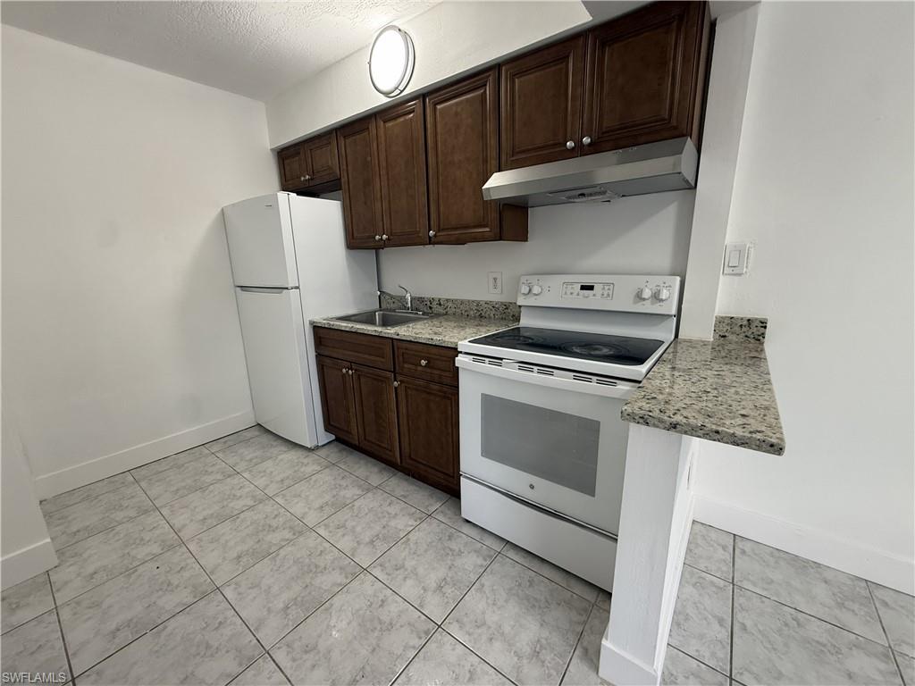 The kitchen features white appliances, dark wooden cabinetry, granite countertops, and tile flooring