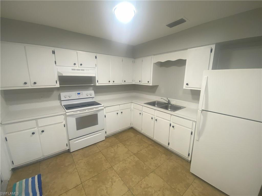 Kitchen featuring white appliances, light countertops, white cabinets, under cabinet range hood, and dark tile patterned floors