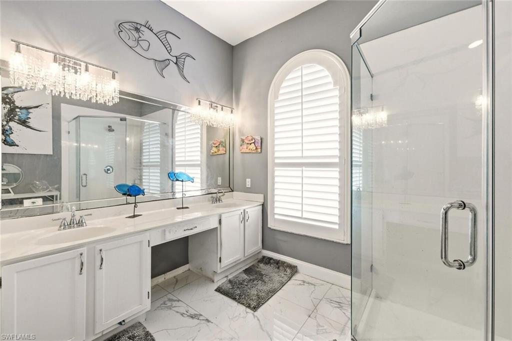 Bathroom with a marble finish shower, double vanity, and light marble finish flooring