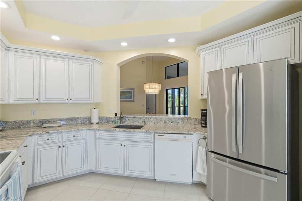 Kitchen featuring white appliances, a chandelier, recessed lighting, white cabinets, and light stone counters