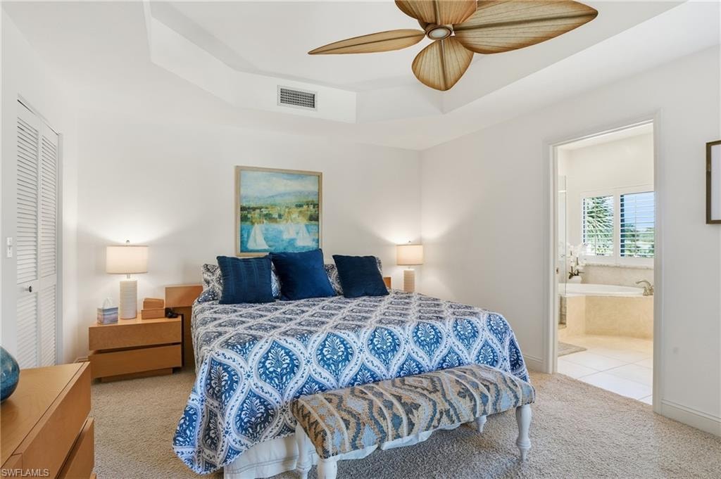 Bedroom with carpet floors, a raised ceiling, a ceiling fan, ensuite bathroom, and a closet