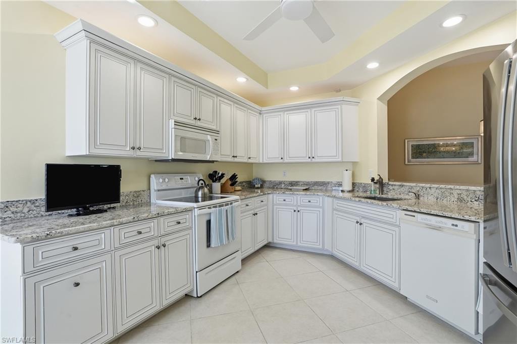 Kitchen with white appliances, light stone counters, recessed lighting, white cabinetry, and a tray ceiling