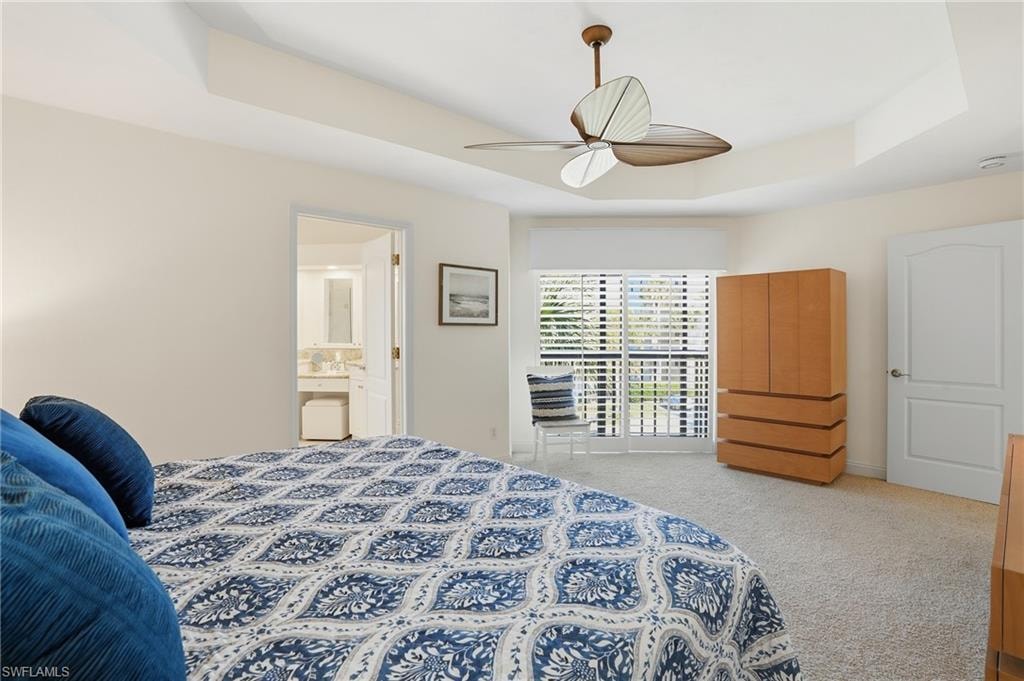 Bedroom featuring light colored carpet, a tray ceiling, a ceiling fan, ensuite bath, and access to outside