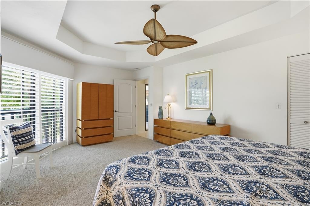 Bedroom with light colored carpet, a ceiling fan, a tray ceiling, and access to exterior