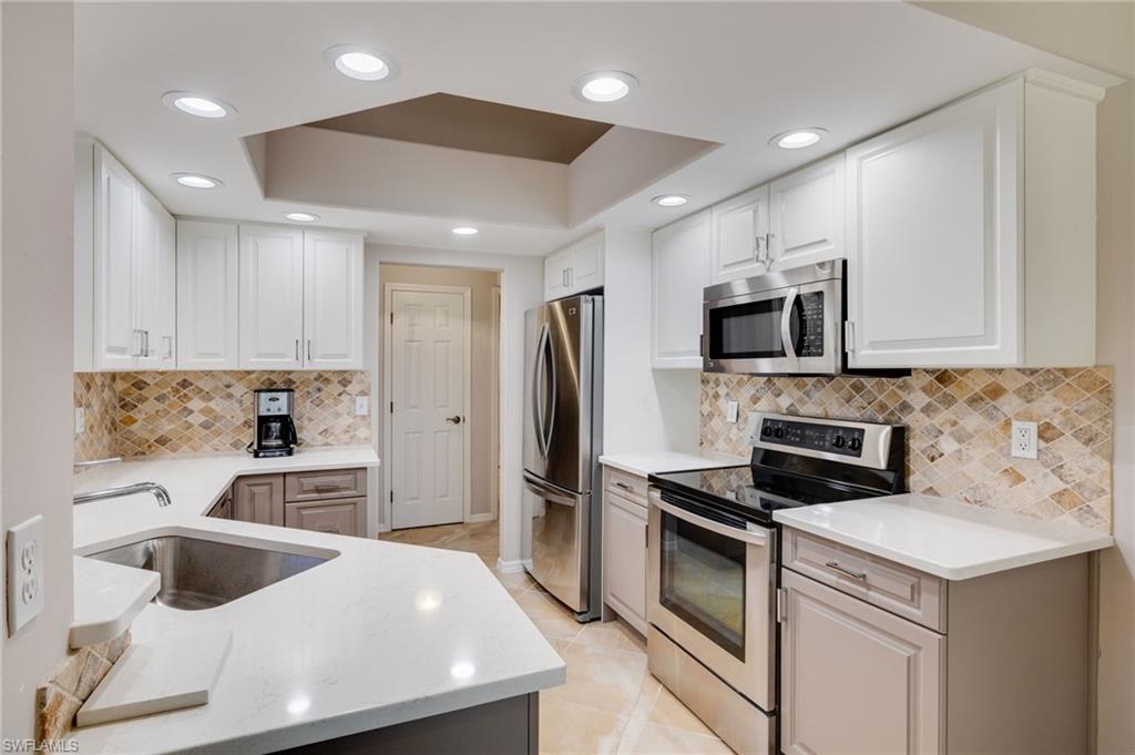 Kitchen with stainless steel appliances, recessed lighting, white cabinetry, a tray ceiling, and quartz countertops