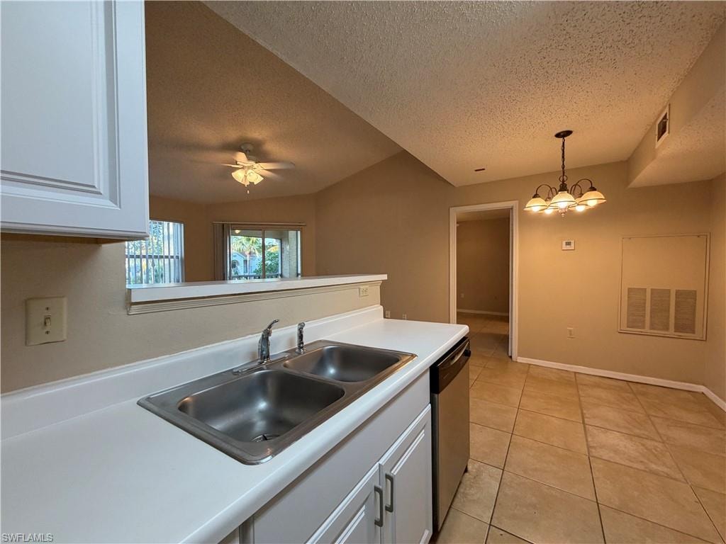 Kitchen with white cabinets, light countertops, pendant lighting, a textured ceiling, and stainless steel dishwasher