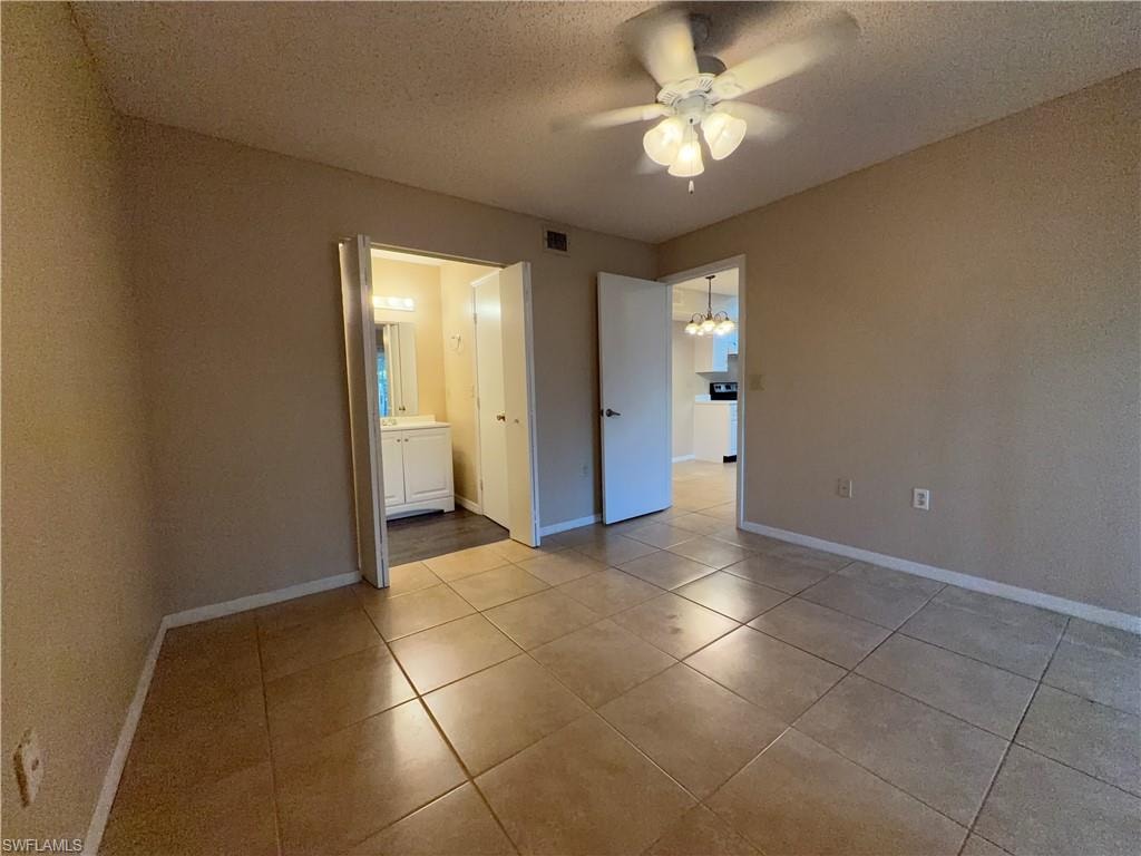 Unfurnished bedroom with a textured ceiling, a chandelier, ceiling fan, light tile patterned floors, and connected bathroom