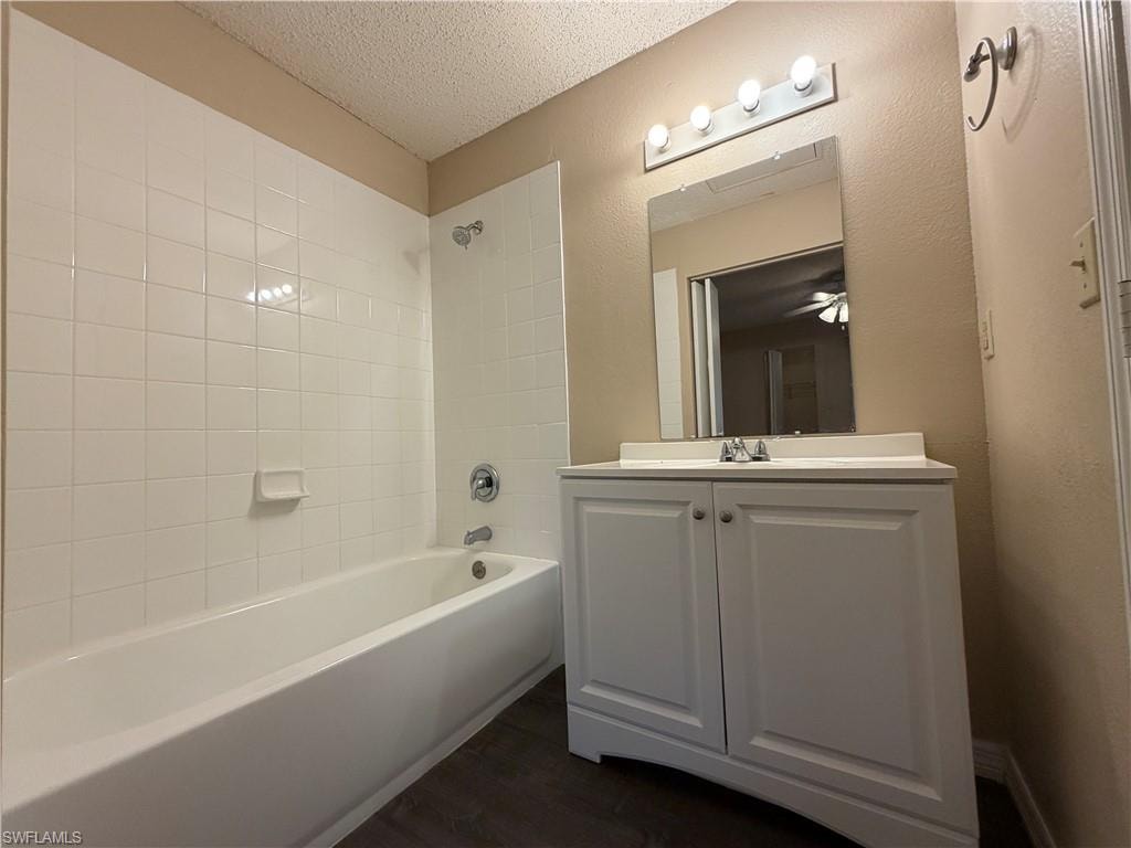 Full bathroom with vanity, washtub / shower combination, a textured ceiling, dark wood finished floors, and a textured wall