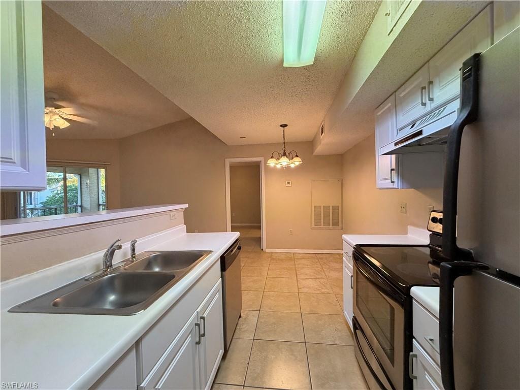 Kitchen with appliances with stainless steel finishes, under cabinet range hood, a textured ceiling, light countertops, and pendant lighting