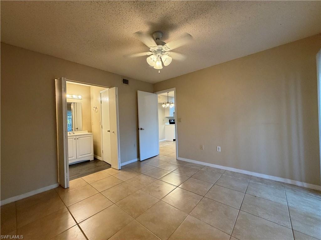 Unfurnished bedroom featuring a textured ceiling, ceiling fan, a chandelier, light tile patterned floors, and connected bathroom