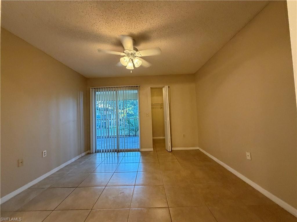 Tiled empty room with a textured ceiling and a ceiling fan
