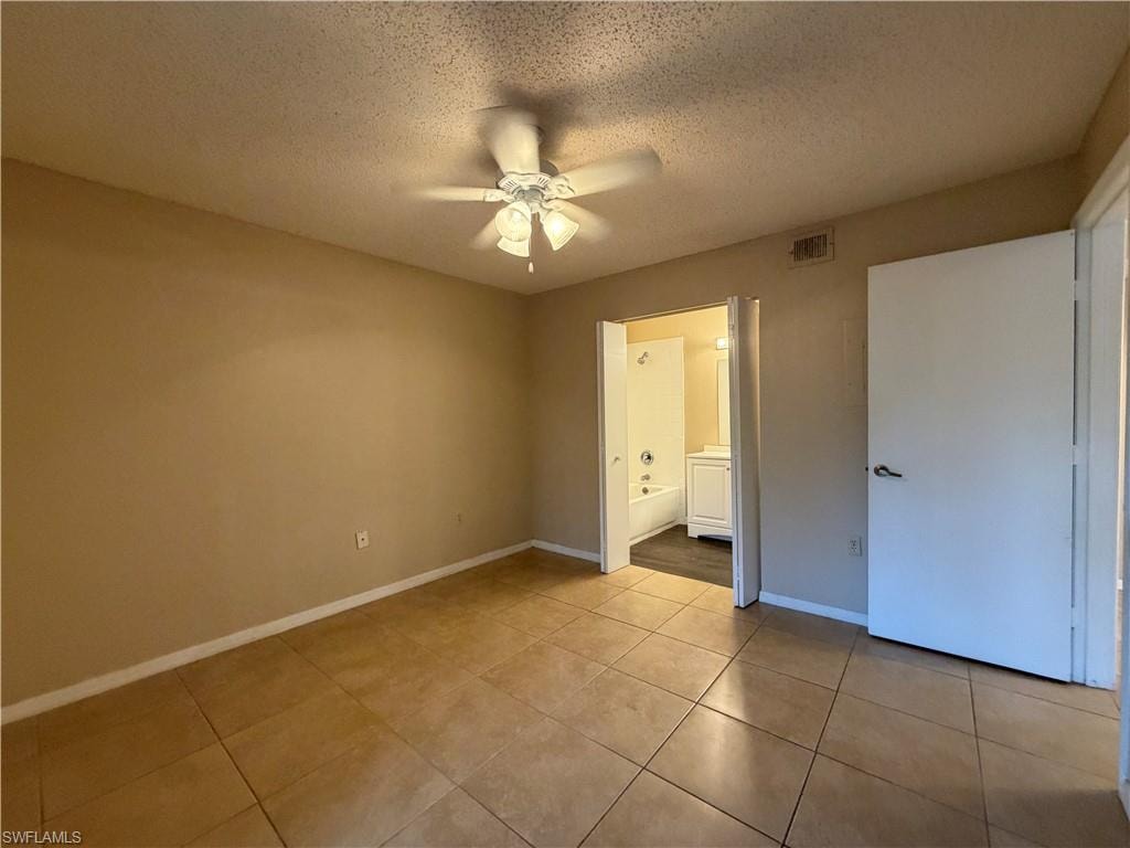 Unfurnished bedroom featuring a textured ceiling, a ceiling fan, connected bathroom, and light tile patterned floors