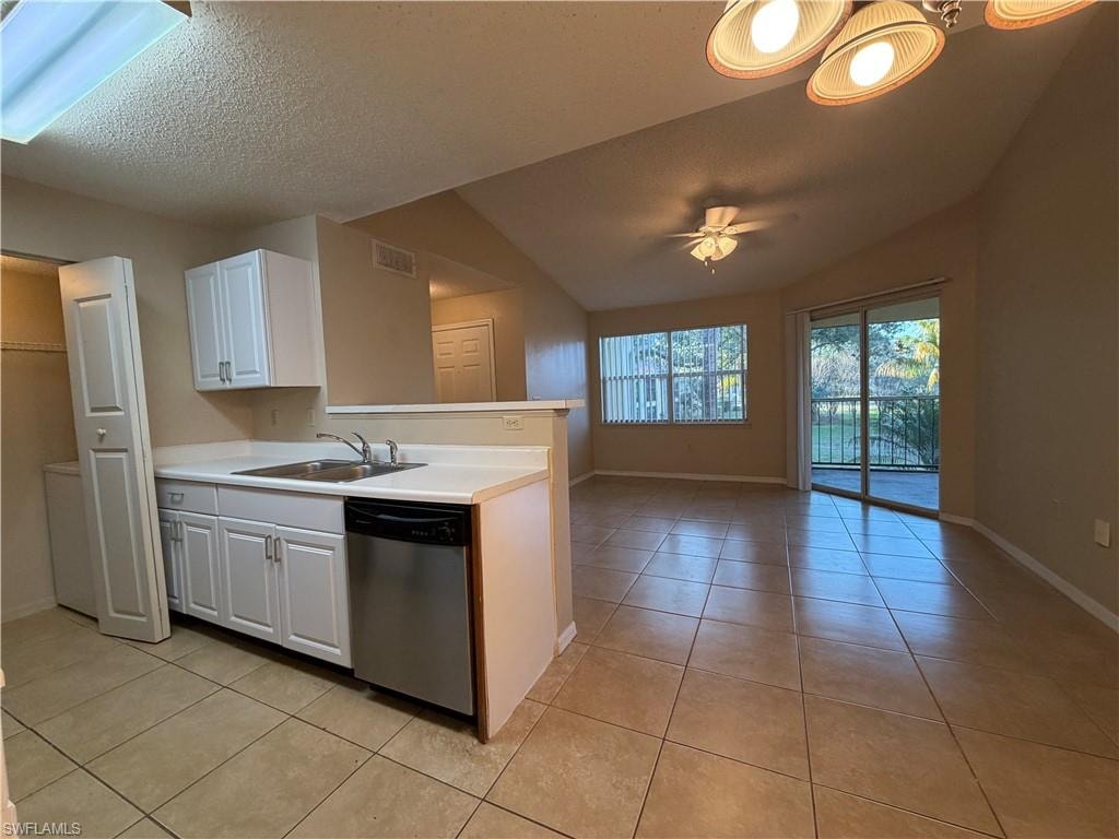 Kitchen with a textured ceiling, stainless steel dishwasher, vaulted ceiling, white cabinetry, and light tile patterned floors