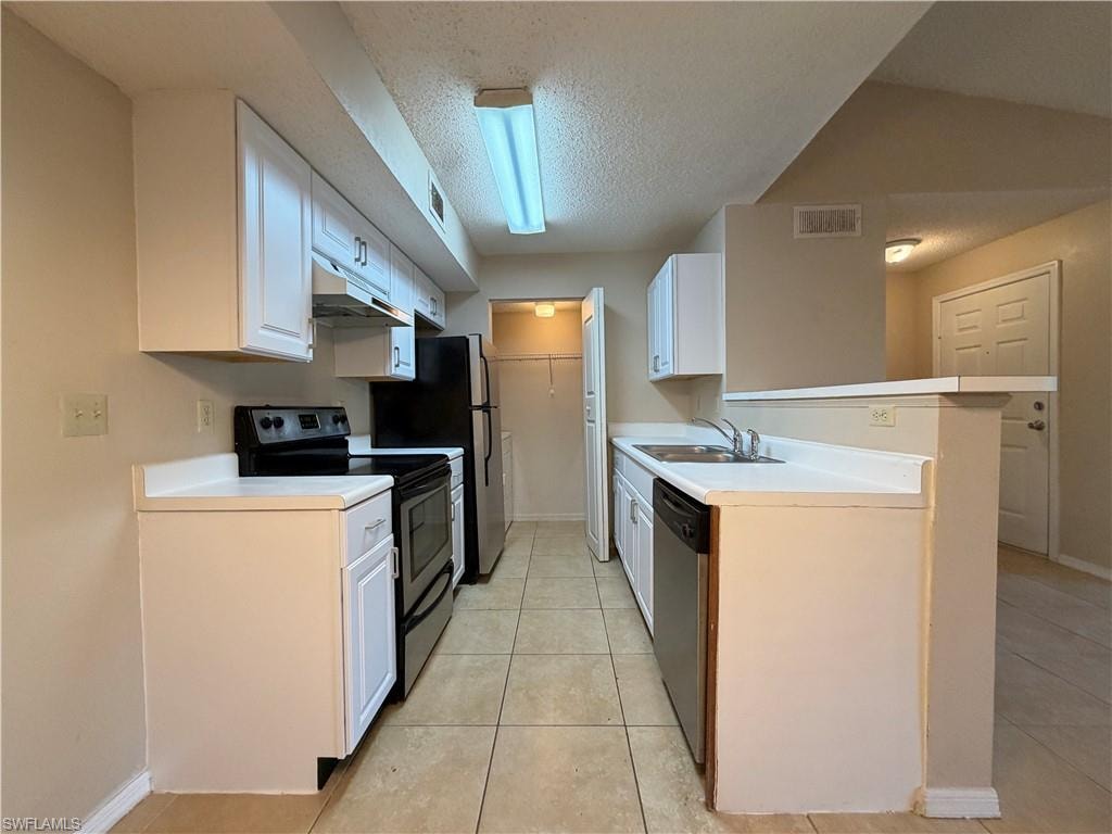 Kitchen with appliances with stainless steel finishes, a textured ceiling, white cabinets, and light countertops