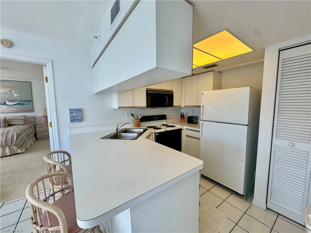 Kitchen with white appliances, light countertops, a peninsula, a kitchen breakfast bar, and light tile flooring