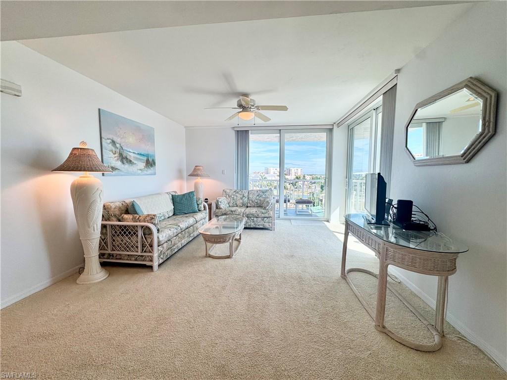 Living area featuring a wall of windows, ceiling fan, and light colored carpet