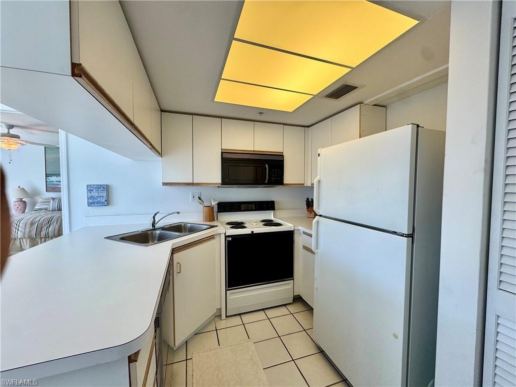 Kitchen with white appliances, light countertops, white cabinets, a peninsula, and light tile  floors