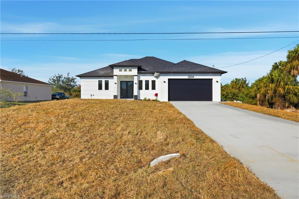 Prairie-style home featuring concrete driveway, an attached garage, stucco siding, a front lawn, and a shingled roof