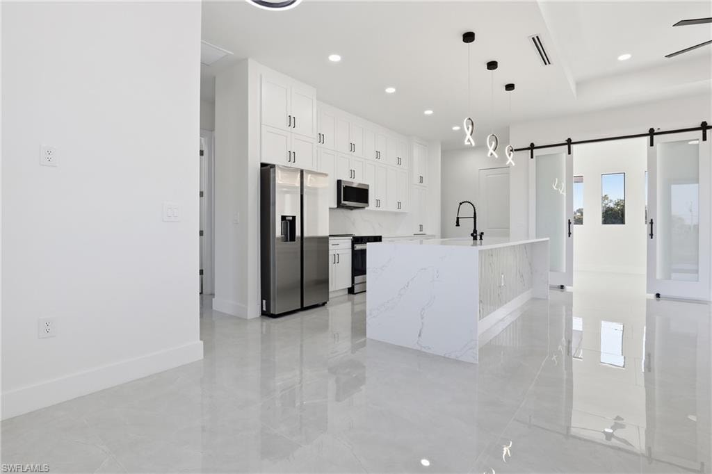 Kitchen with stainless steel appliances, white cabinetry, a barn door, decorative light fixtures, and light stone counters