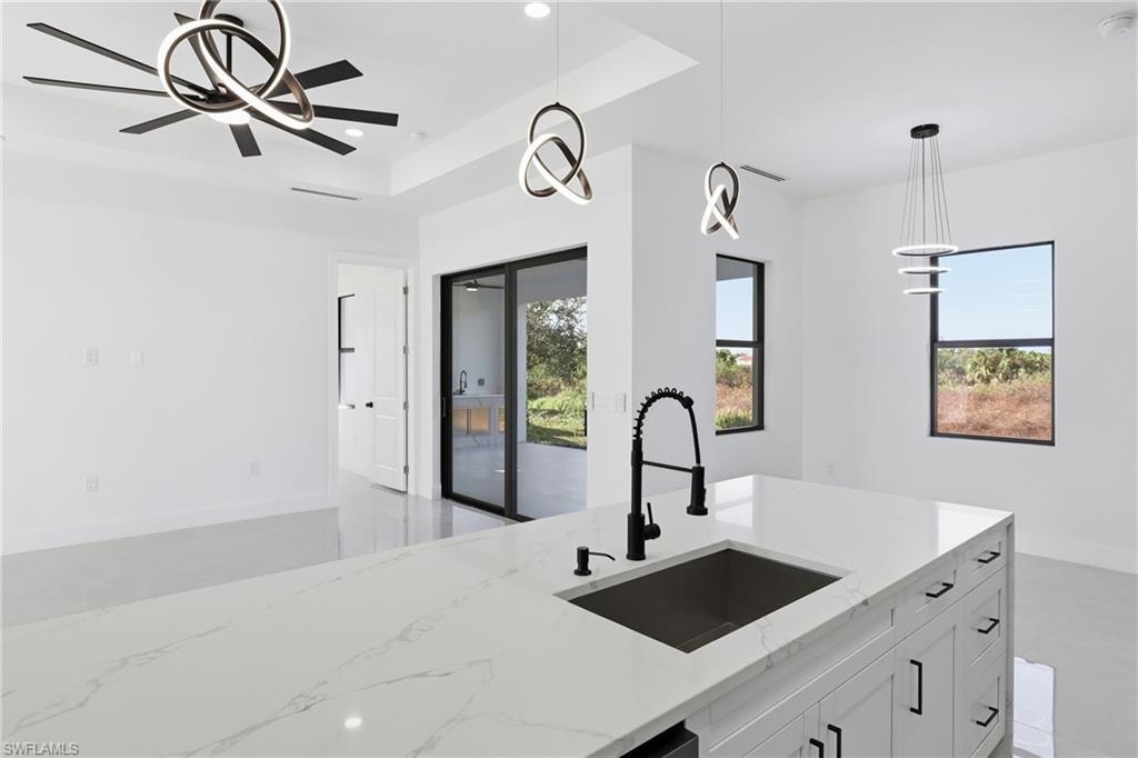 Kitchen with decorative light fixtures, light stone countertops, white cabinets, plenty of natural light, and recessed lighting