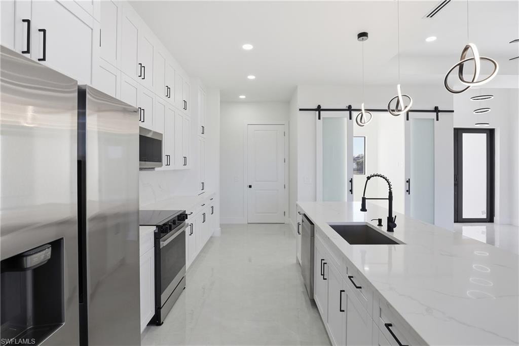 Kitchen featuring appliances with stainless steel finishes, white cabinets, light stone countertops, a barn door, and pendant lighting