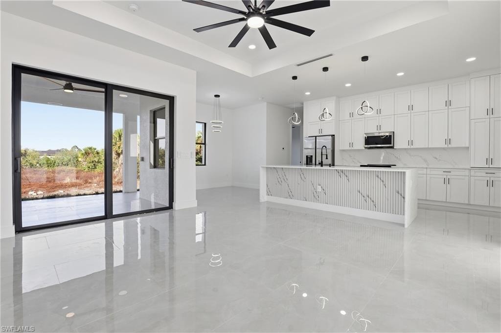 Kitchen featuring a raised ceiling, a ceiling fan, an island with sink, white cabinetry, and recessed lighting