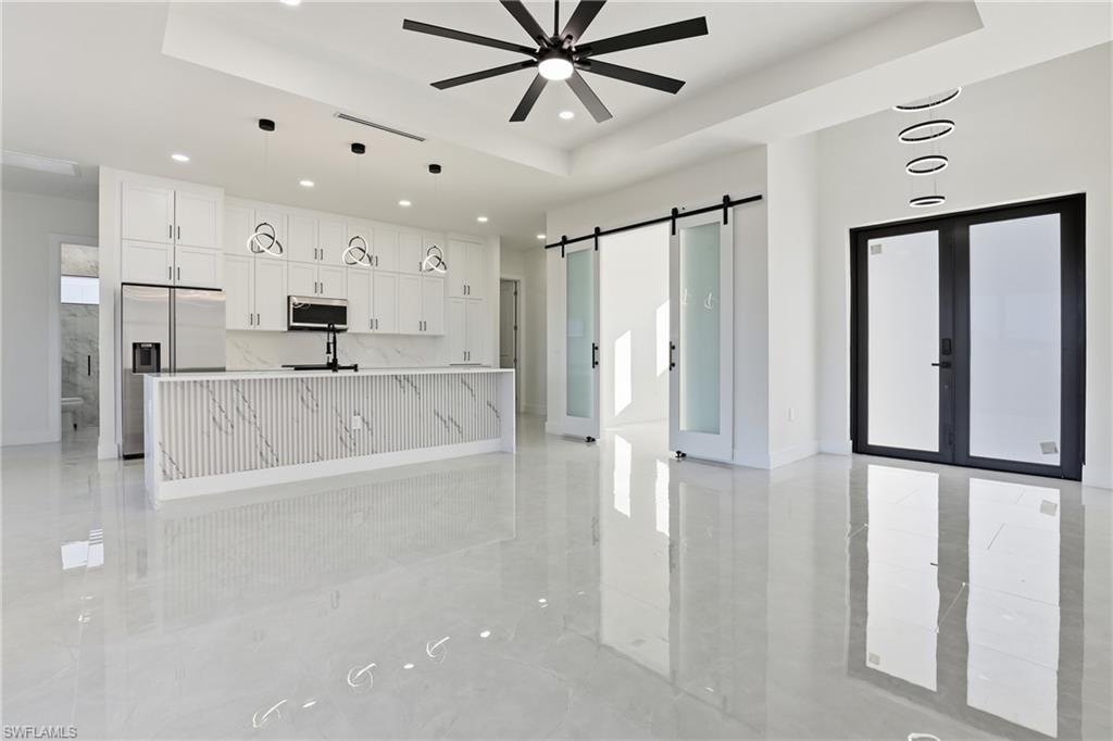 Kitchen featuring white cabinets, a raised ceiling, appliances with stainless steel finishes, an island with sink, and recessed lighting