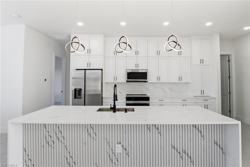 Kitchen featuring light stone counters, stainless steel appliances, decorative backsplash, white cabinets, and recessed lighting