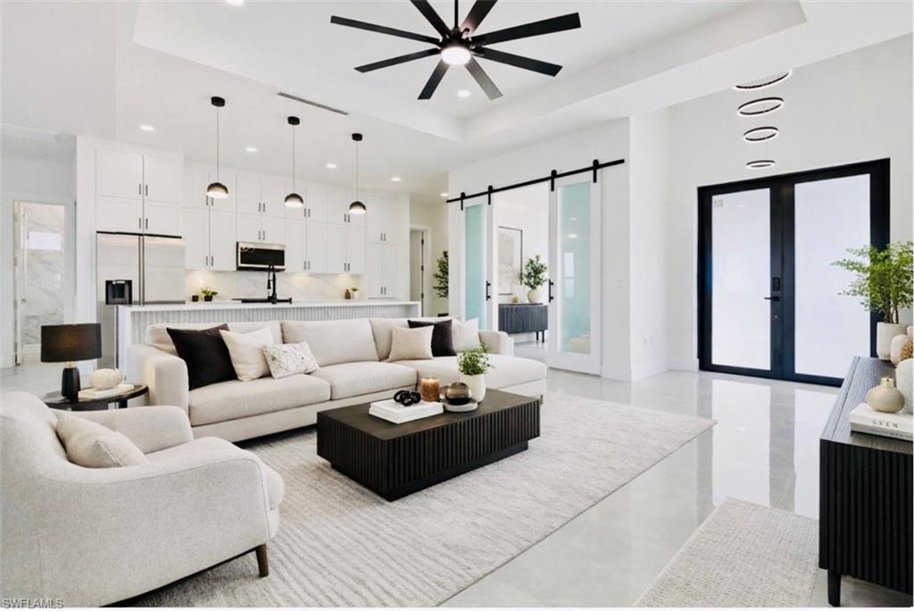 Living area featuring a barn door, a raised ceiling, a ceiling fan, french doors, and recessed lighting. Digitally Staged.