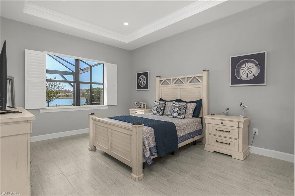 spacious primary bedroom features amazing lake views, tray ceiling with decorative crown molding, plantation shutters, and ensuite spa-like bath.