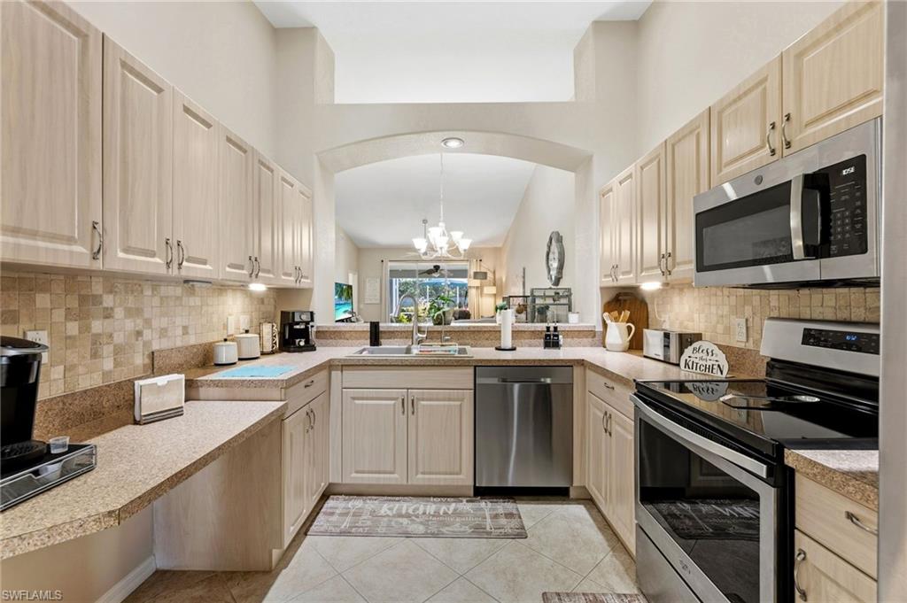 Kitchen featuring stainless steel appliances, a chandelier, pendant lighting, light tile patterned flooring, and light countertops