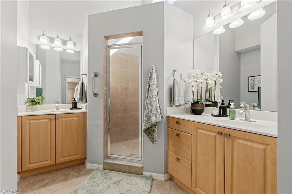 Bathroom featuring a stall shower, two vanities, and light tile patterned floors