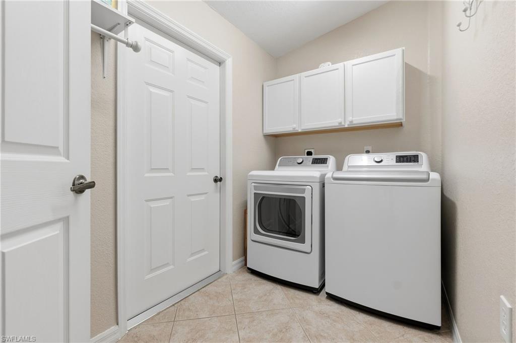 Washroom with washer and clothes dryer, light tile patterned floors, cabinet space, and a textured wall