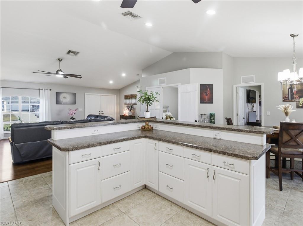 Kitchen featuring open floor plan, white cabinetry, a ceiling fan, pendant lighting, and vaulted ceiling