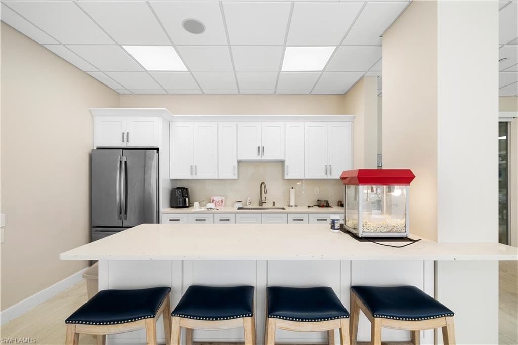Kitchen with a breakfast bar, a drop ceiling, white cabinets, light stone countertops, and tasteful backsplash