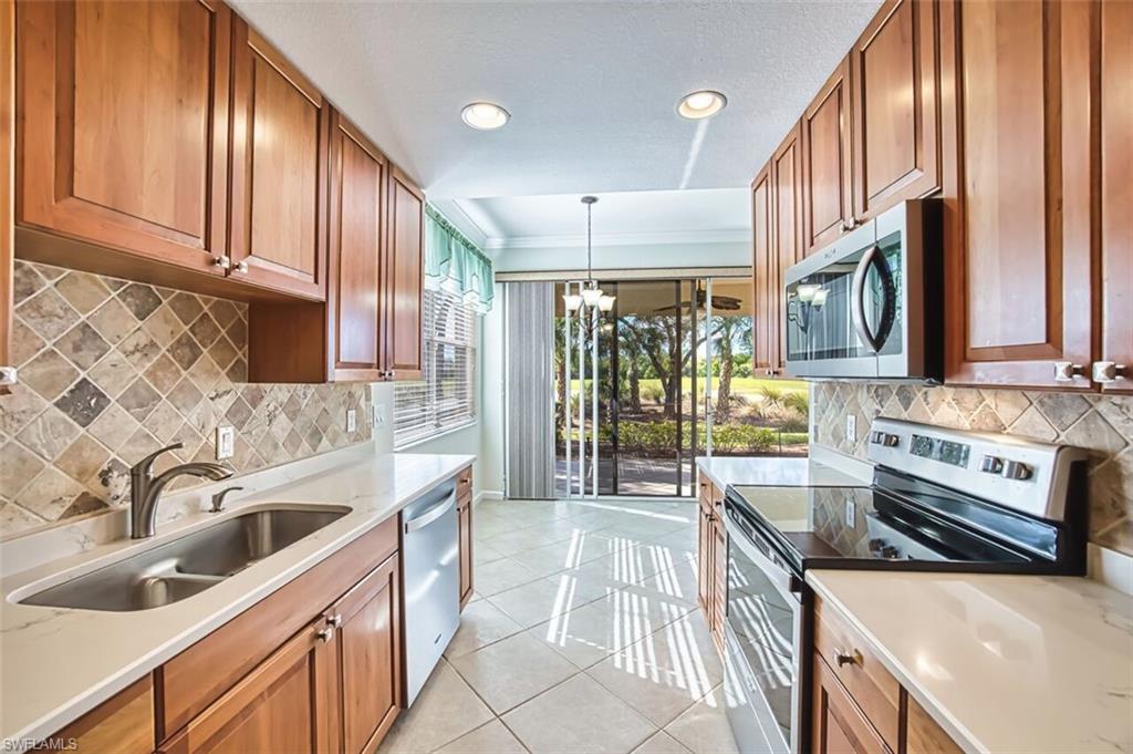 Kitchen featuring stainless steel appliances, brown cabinets, light tile patterned floors, tasteful backsplash, and hanging light fixtures