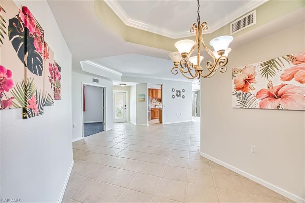 Unfurnished dining area with ornamental molding, a raised ceiling, a chandelier, and light tile patterned floors
