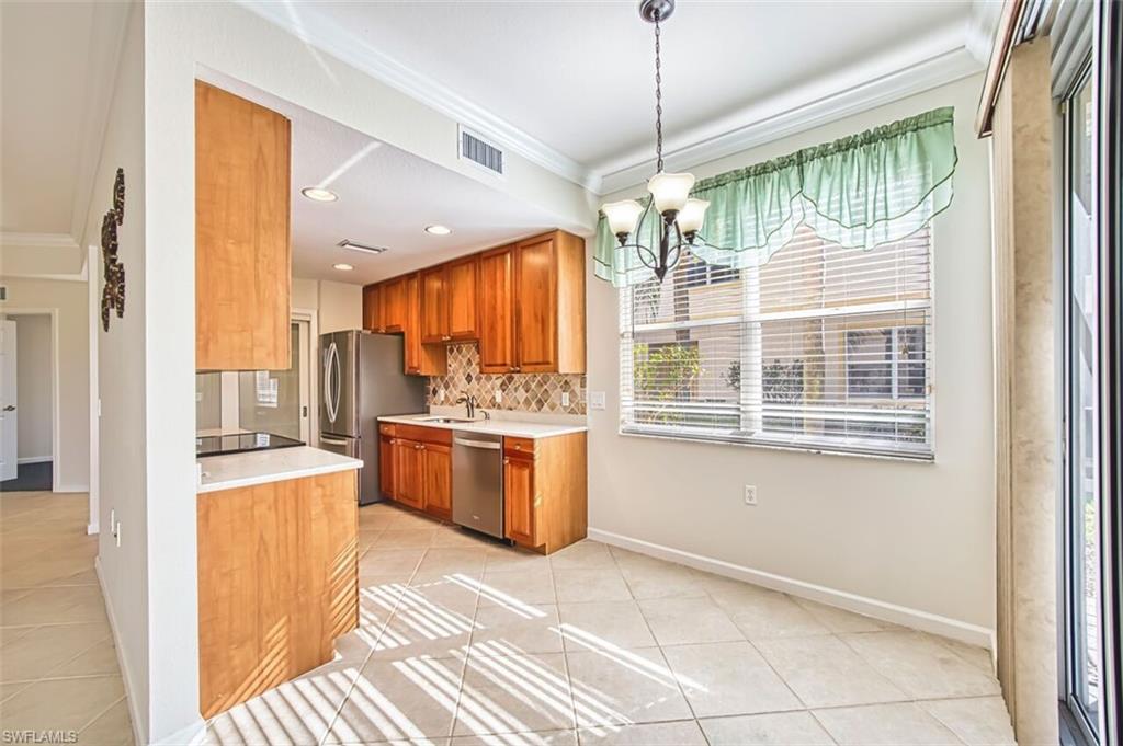 Kitchen with ornamental molding, light tile patterned floors, light countertops, a chandelier, and brown cabinets